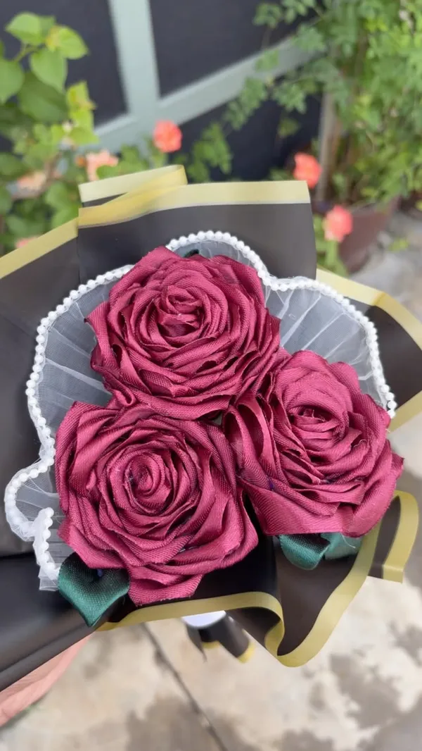 Three large burgundy satin roses with pearl lace and gold-edged black wrap